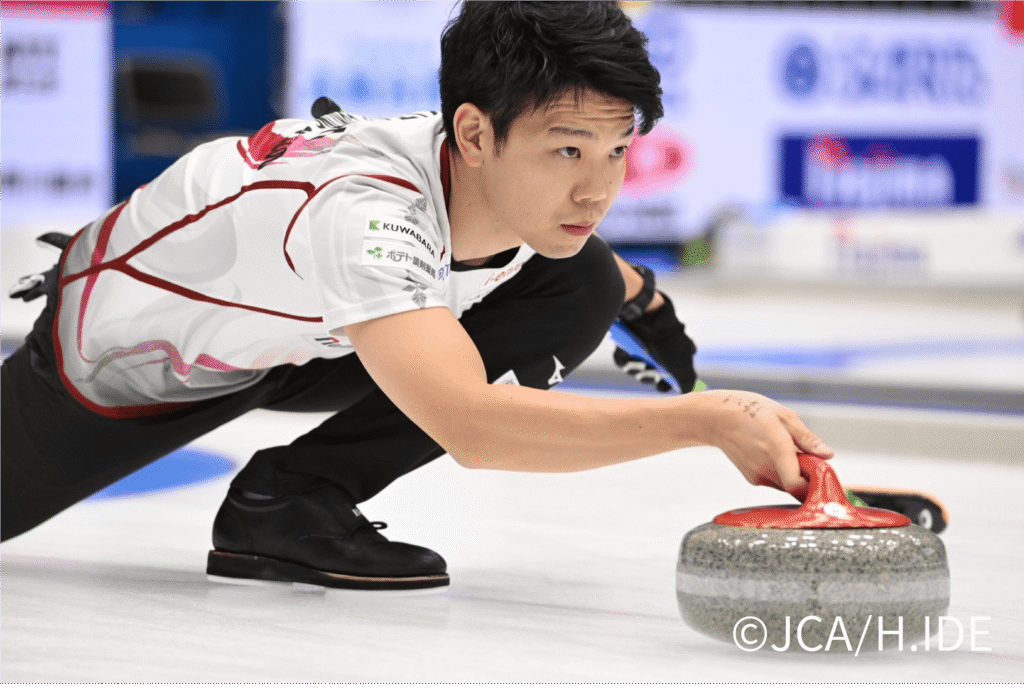 カーリングの試合中、ストーンを持ってプレーする男性