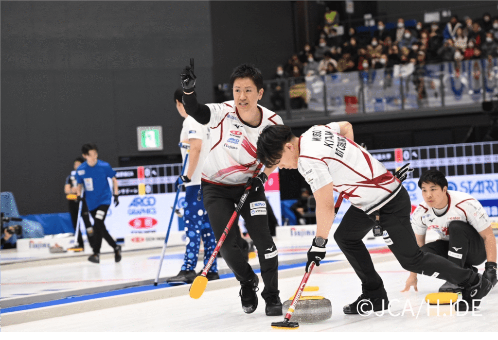 カーリングの試合中、スイープする男性選手と他の選手2人